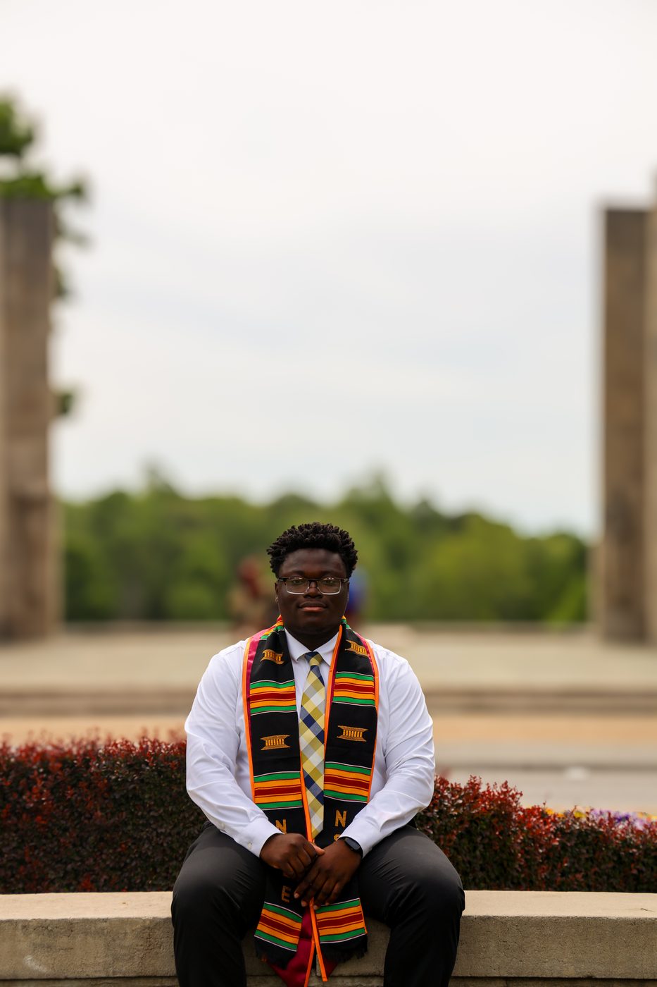 Graduate with kente stole seated at memorial court
