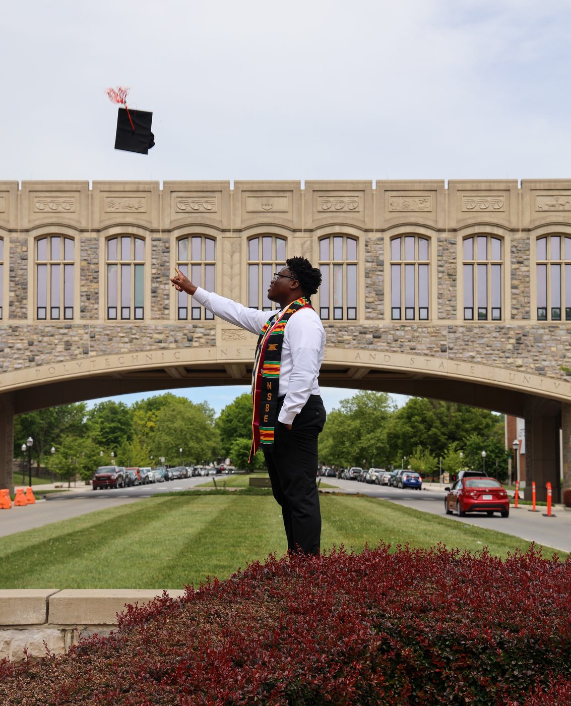 Graduate tossing cap by campus bridge